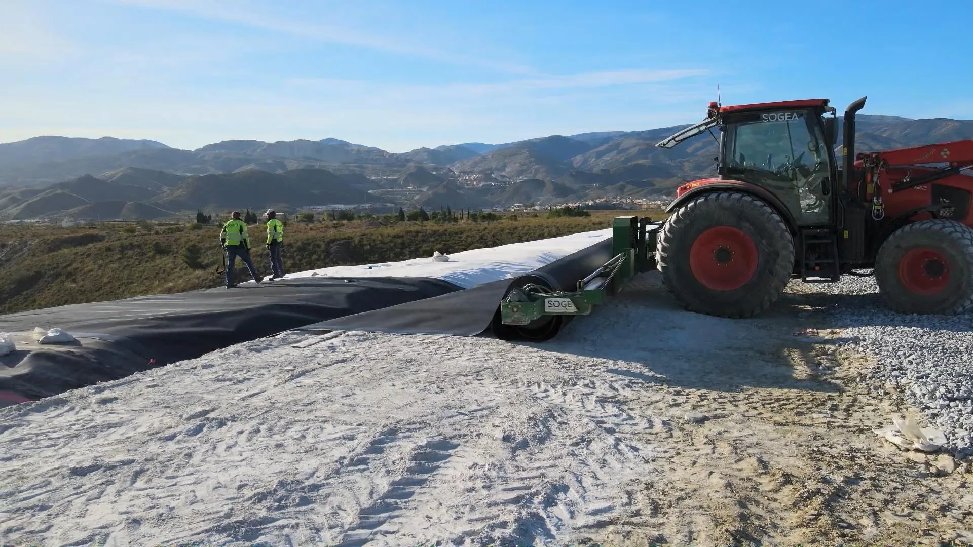 Tractor con desbobinador desplegando geomembrana sobre geotextil